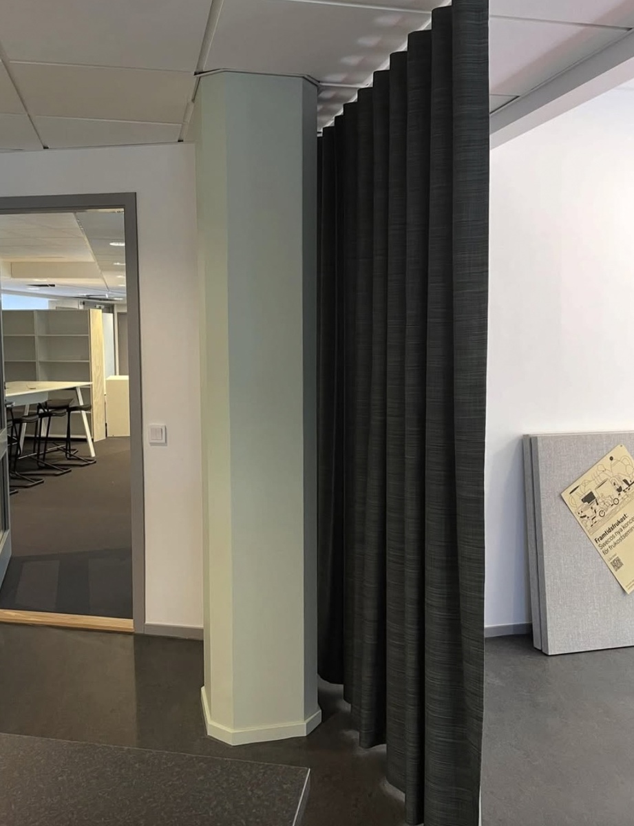 Veckad väggpanel monterad som rumsavskiljare i modern kontorsmiljö.