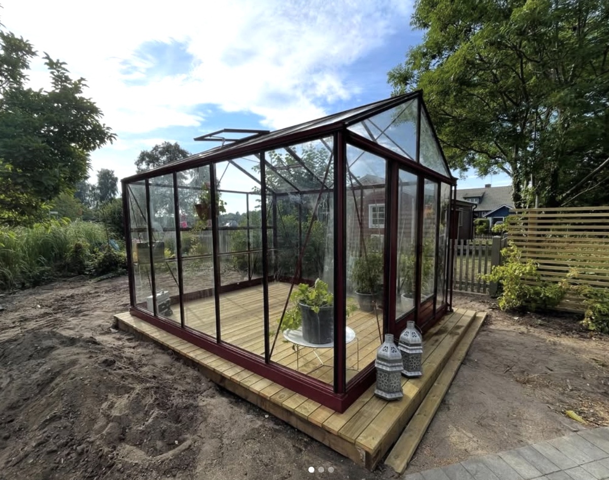Växthus uppfört på nybyggt trädäck i trädgårdsmiljö sett från sidan.