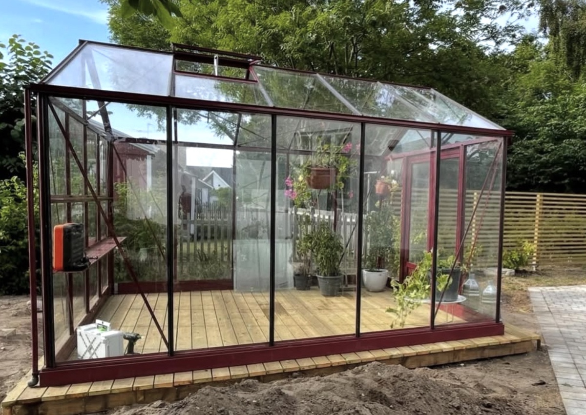 Växthus monterat på nybyggt trädäck i trädgårdsmiljö.