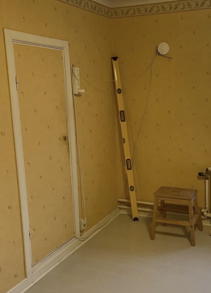 Rum inför renovering med äldre väggbeklädnad och verktyg placerade för förberedande arbete.