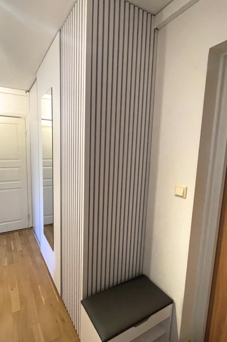 Platsbyggd hallförvaring med ribbpanel, sittbänk och integrerad spegel.