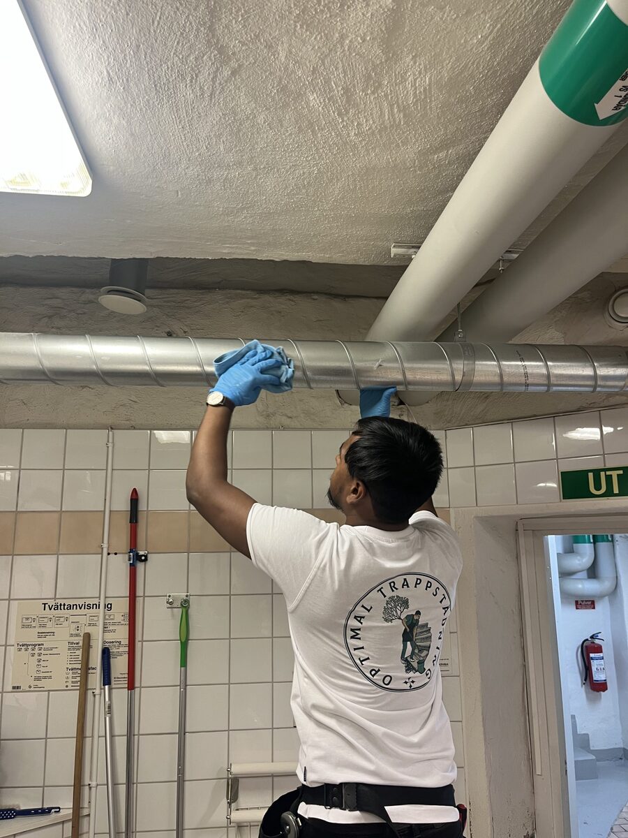 Lokalvårdare rengör rör och tak i gemensamt utrymme i fastighet.