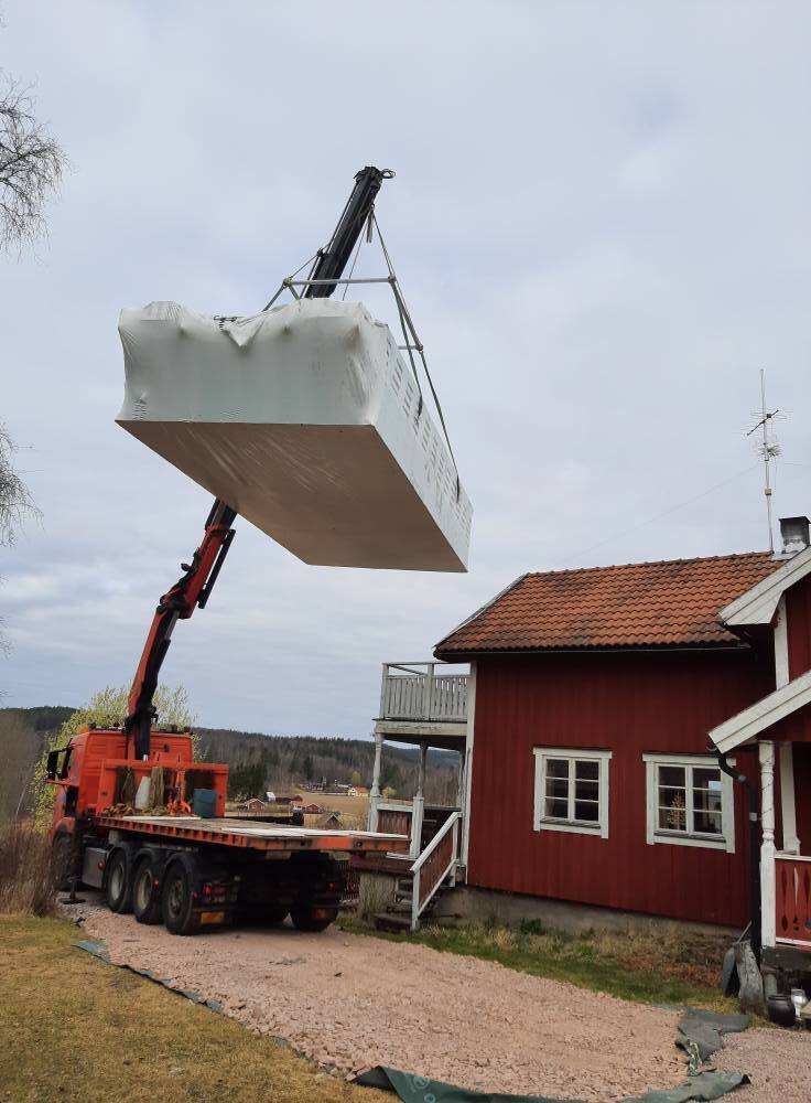 Lyft av betongelement med kranbil vid fastighet där markarbete och grundförberedelser utförs inför byggnation