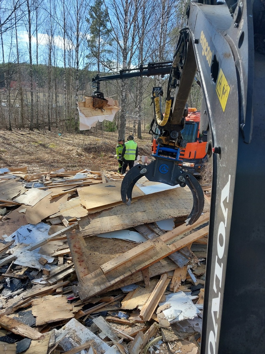 Rivningsarbete med grävmaskin där trä- och byggmaterial sorteras och lyfts bort från arbetsplatsen