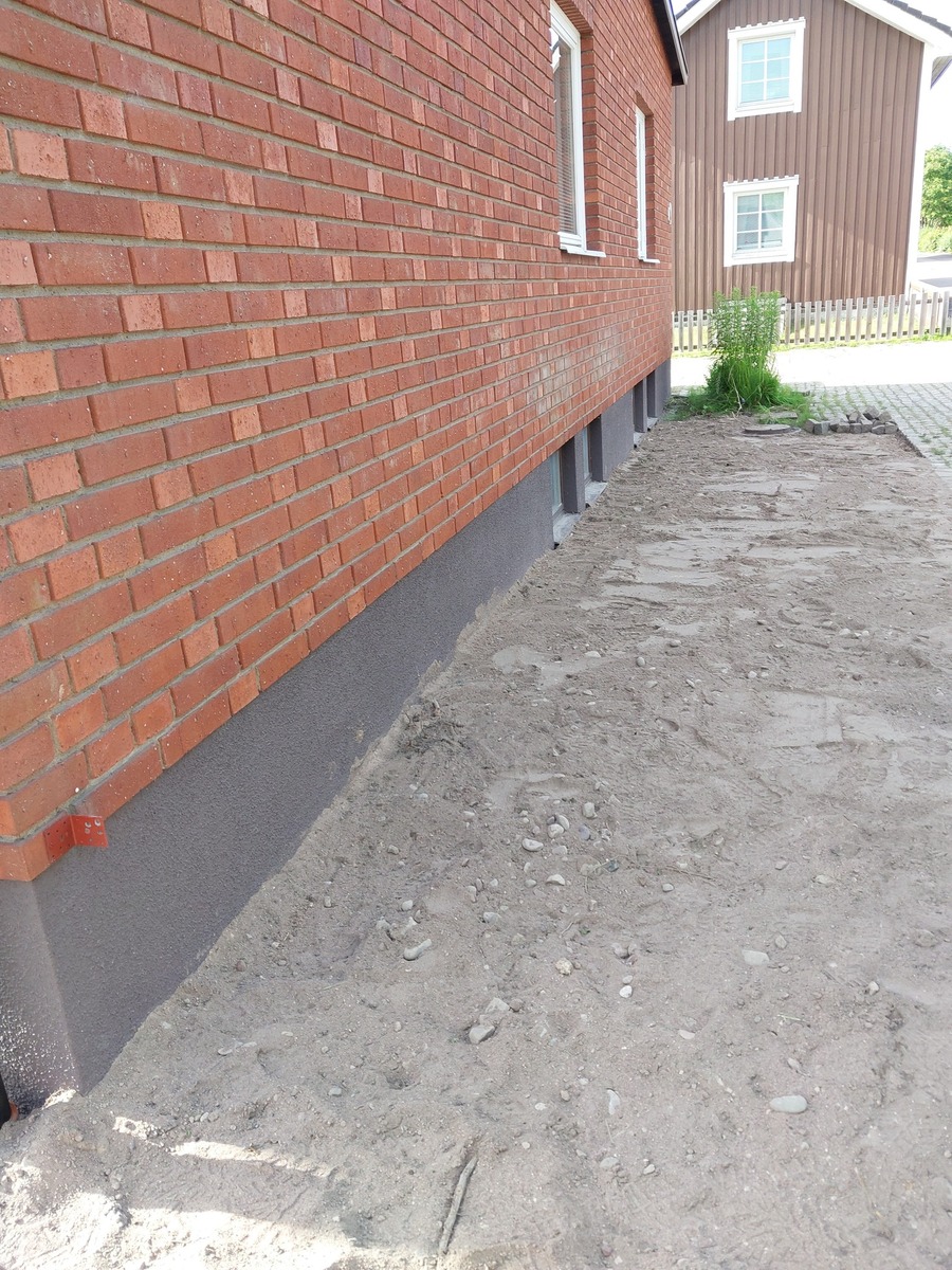 Förberedd mark längs tegelhus där schaktning och grundarbete har utförts inför dränering