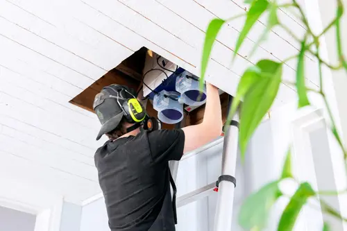 Isolerab-tekniker på stege installerar ventilationssystem i tak genom öppning i innertaket