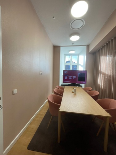 Konferensrum med långt träbord och rosa stolar sett från kortändan
