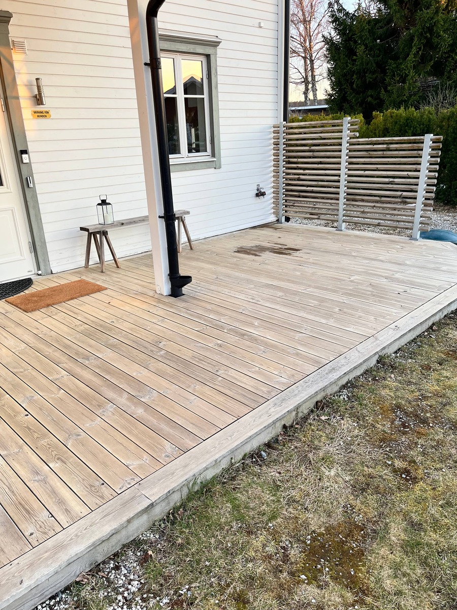 Träterrass vid husentré med nybehandlat trägolv och altan utomhus.