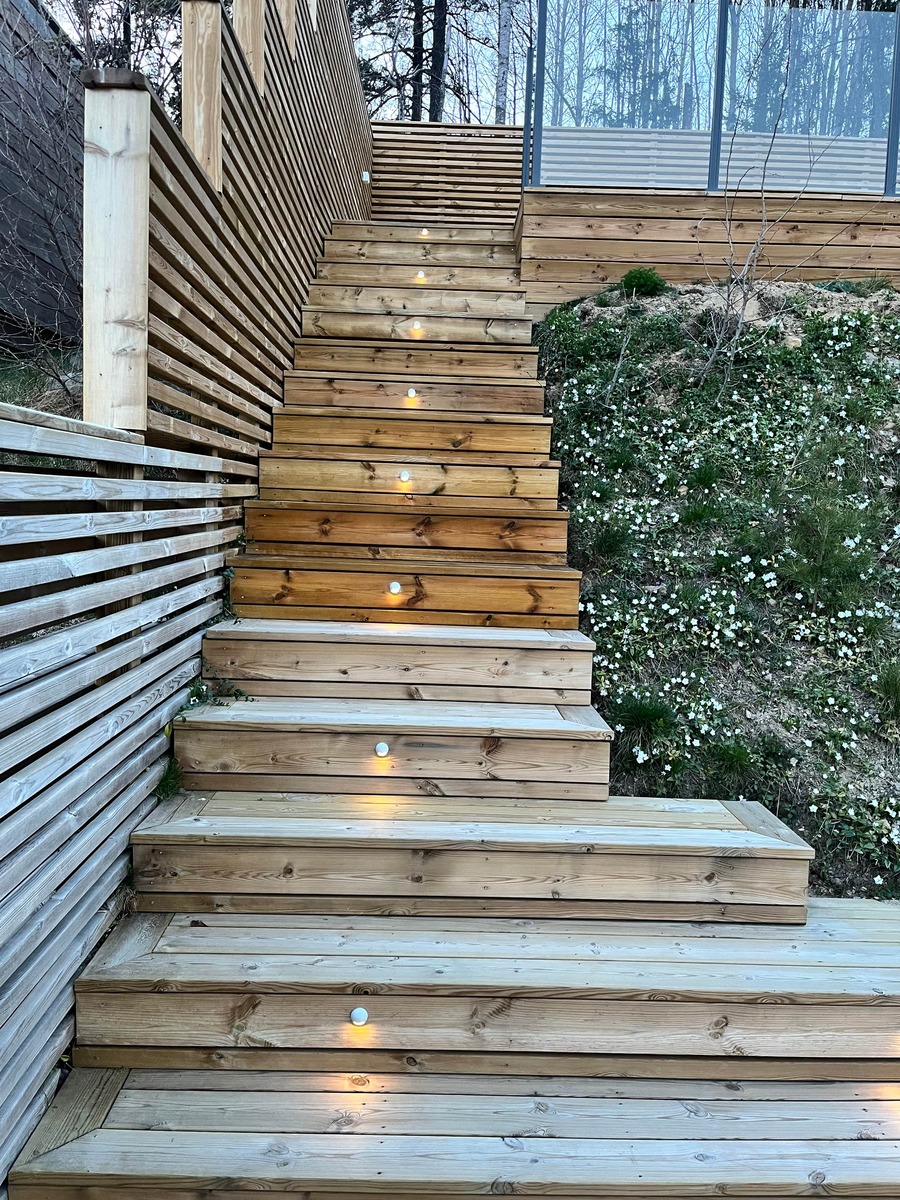 Trätrappa utomhus med nybehandlat trä och infälld belysning.
