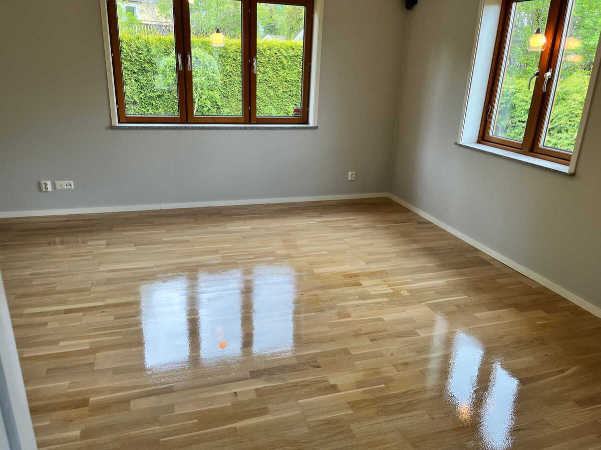 Ljust rum med nylackat parkettgolv och reflektion från fönster.