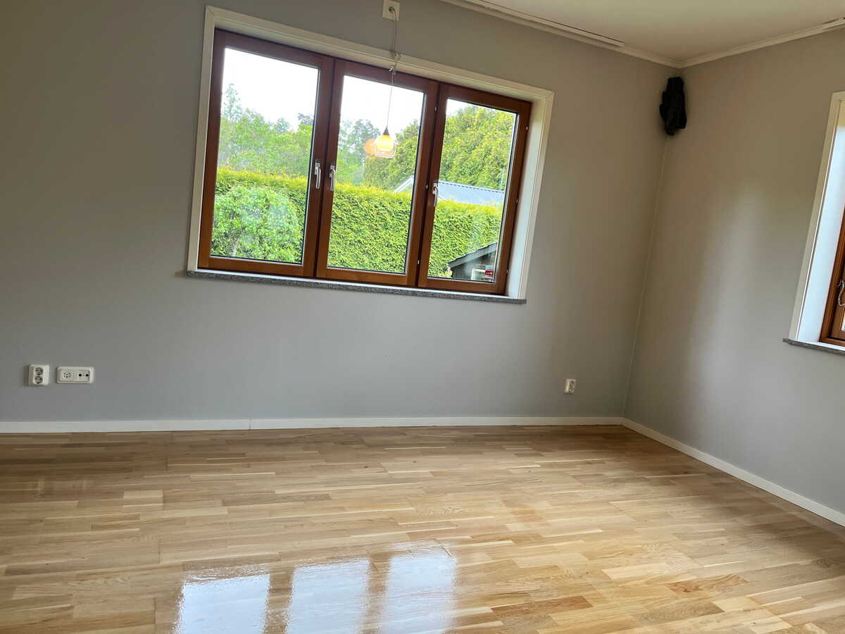 Ljust rum med behandlat parkettgolv och stora fönster.