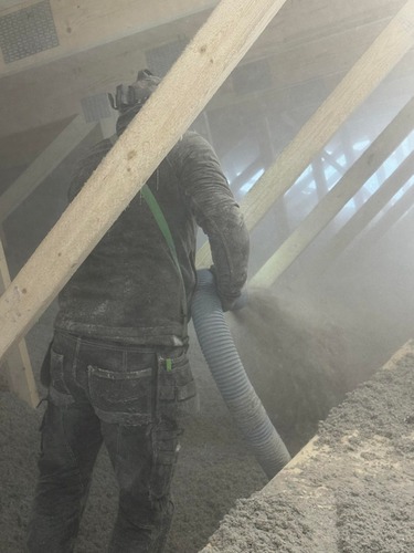 Arbetare som installerar lösullsisolering på vind med isoleringsslang