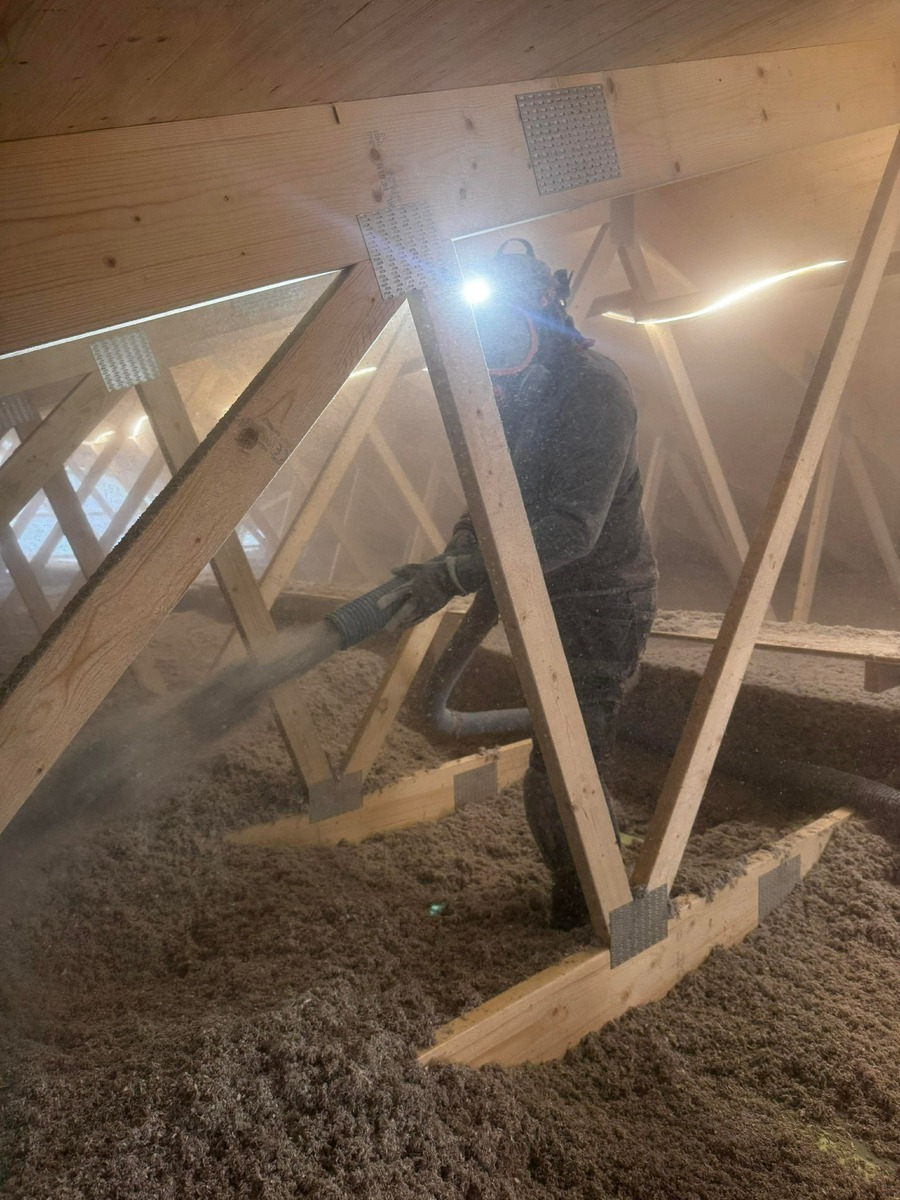 Installatör som blåser lösullsisolering på vind mellan takstolar