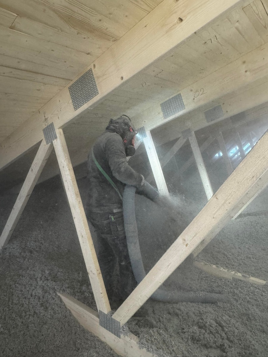 Installatör som sprider lösullsisolering mellan takstolar på vind