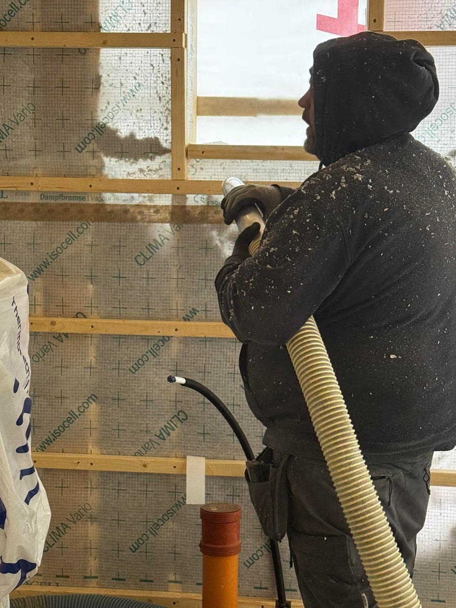 Arbetare som installerar isolering i vägg med lösullsisolering