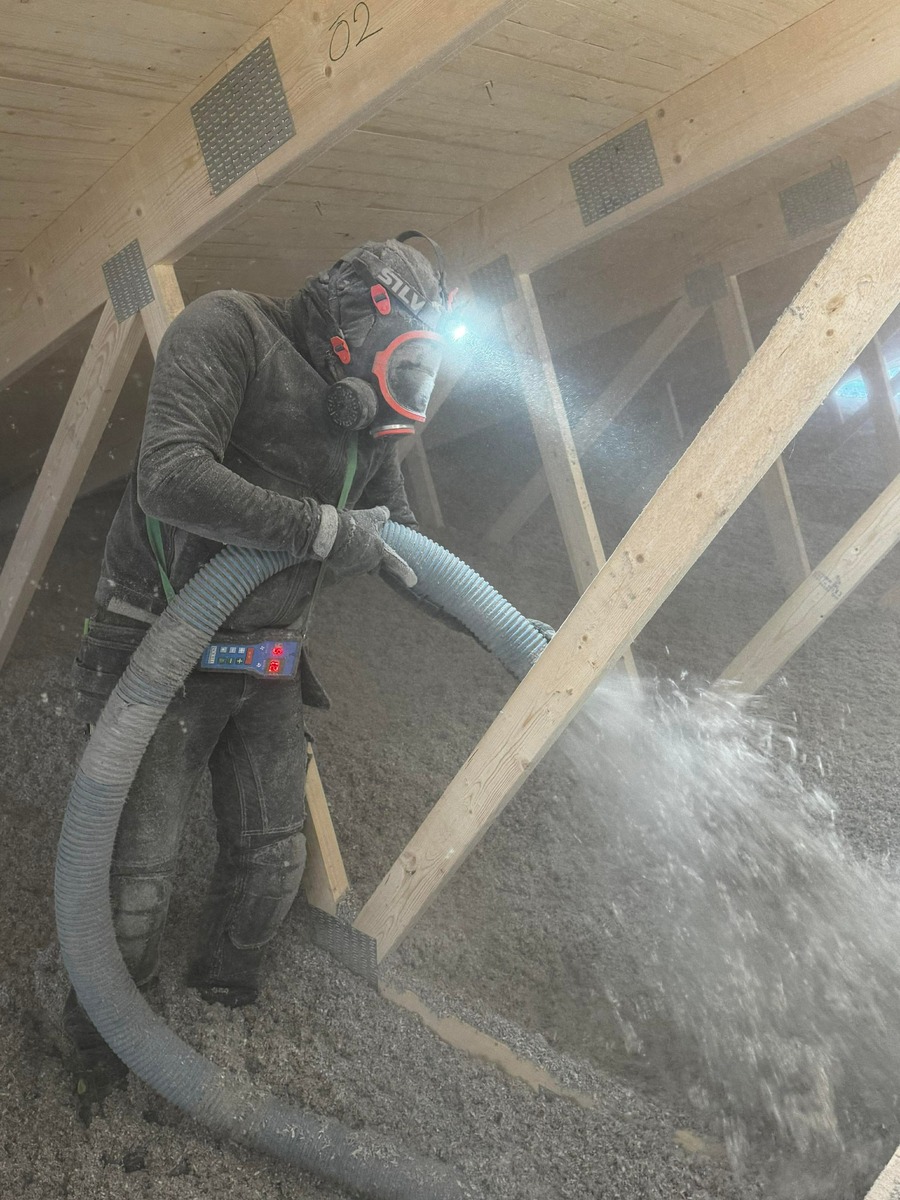Installatör som blåser lösullsisolering på vind mellan takbjälkar