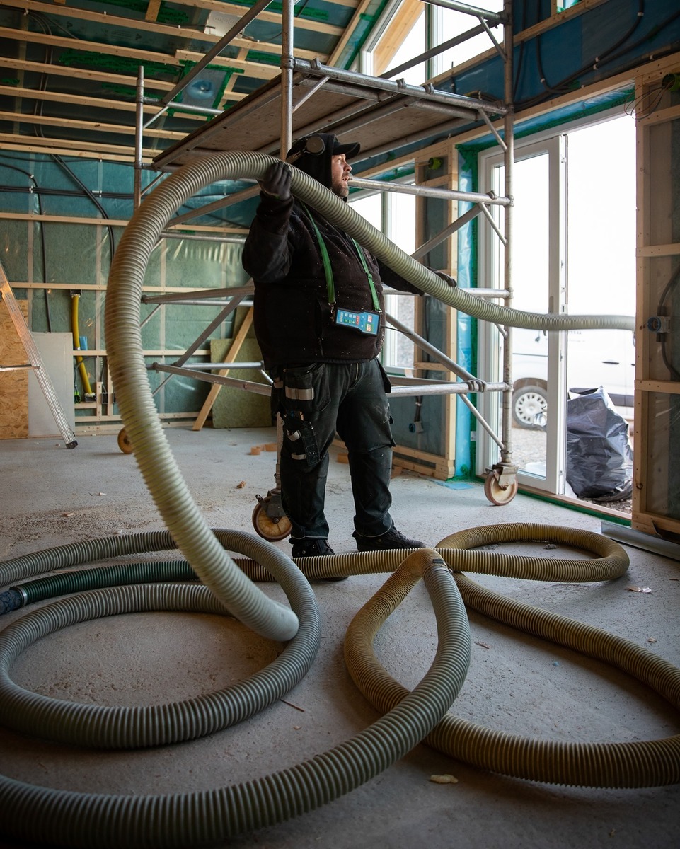 Arbetare som installerar lösullsisolering i byggnad med isoleringsslang