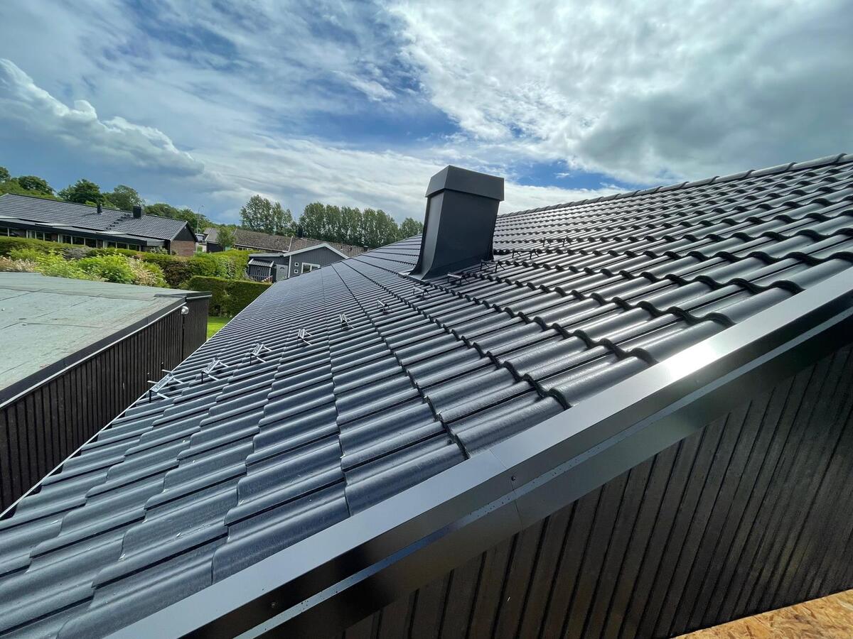 Färdiglagt tak med mörkgrå betongtakpannor och plåtdetaljer på villa