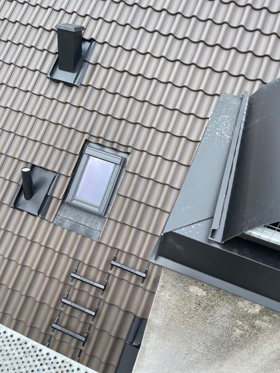 Färdiglagt tak med beige tegelpannor, takfönster och rörgenomföring på villa