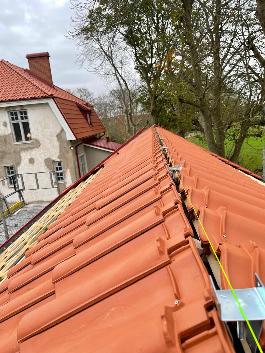 Takläggning med terrakottafärgade tegelpannor på äldre villa med byggställning längs takfoten