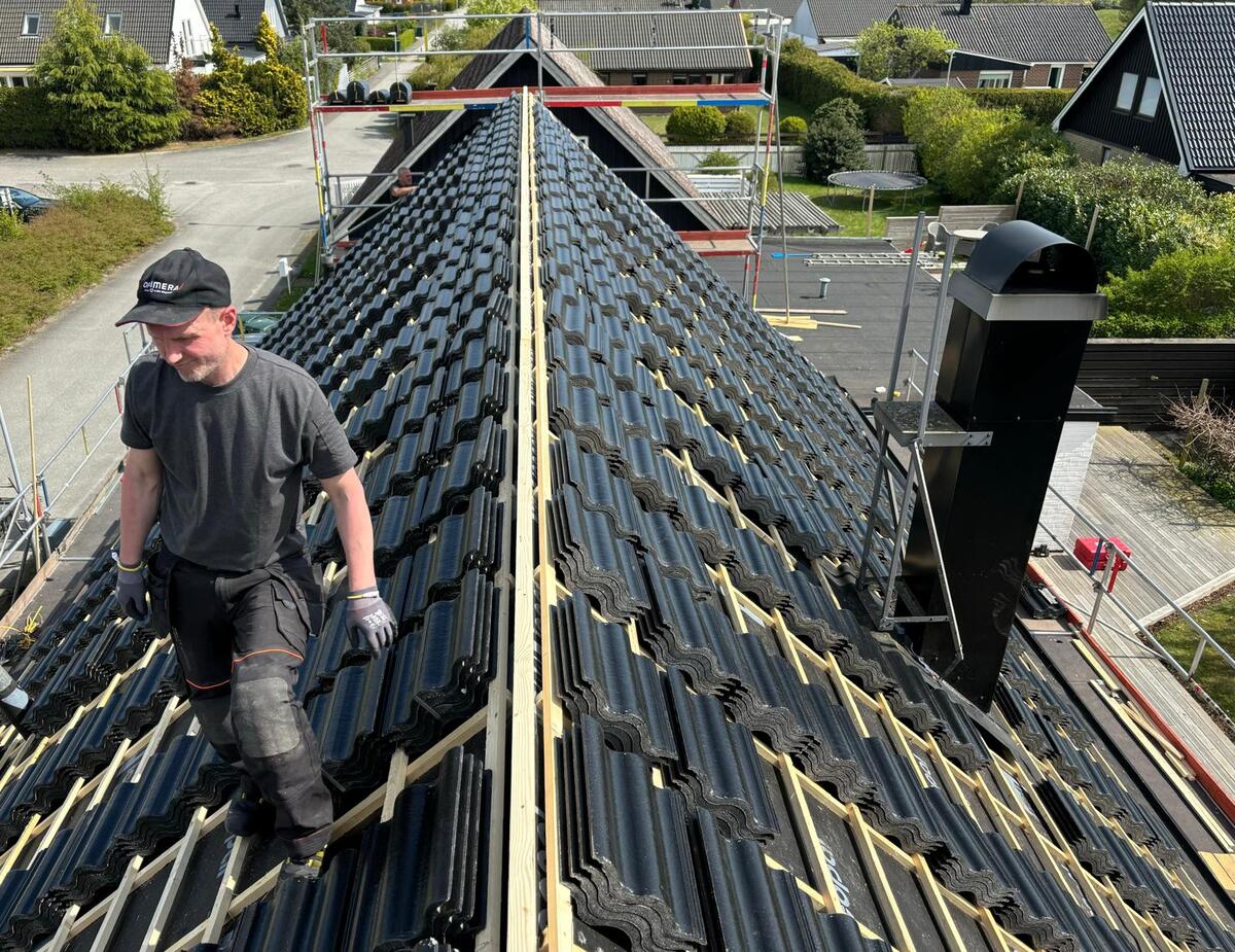 Takläggare arbetar längs nocken på ett tak med svarta betongtakpannor under pågående takläggning