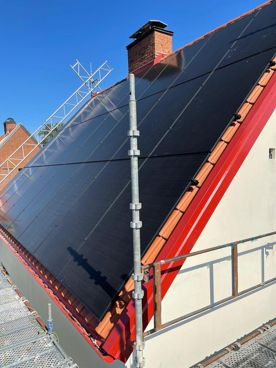 Solpaneler monterade på svart tak med röda plåtdetaljer och byggställning