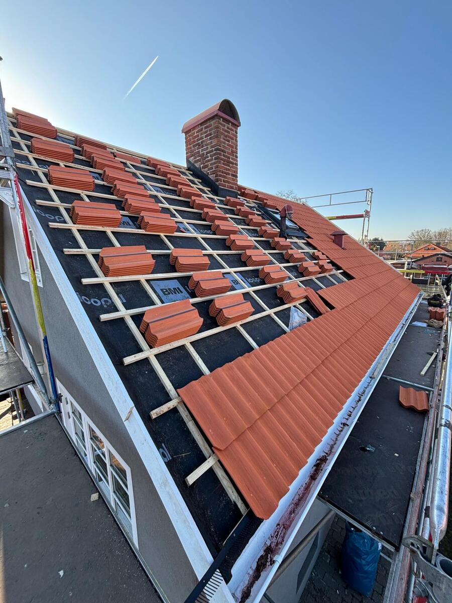 Röda tegelpannor staplade på läkt under pågående takläggning med byggställning längs fasaden