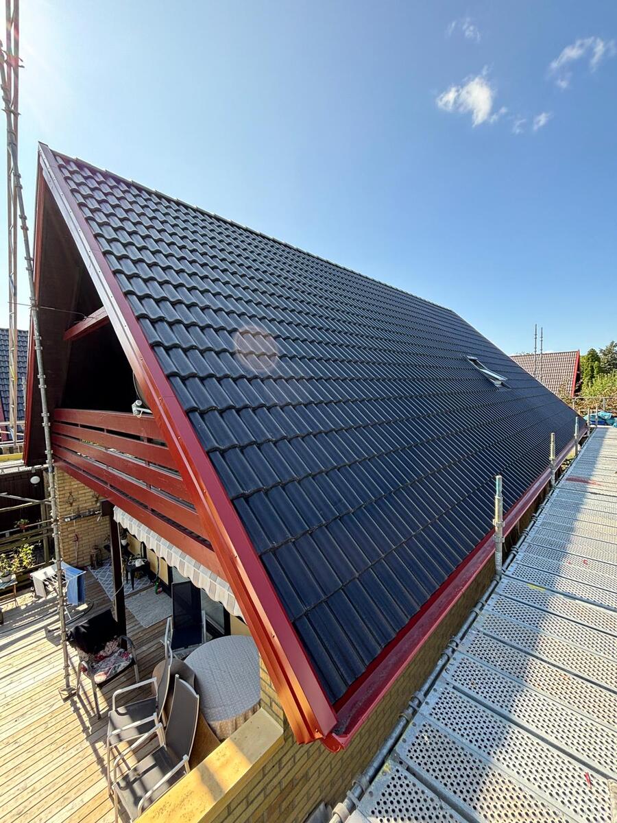 Färdiglagt tak med svarta betongtakpannor och röda plåtdetaljer längs taknock på kommersiell byggnad
