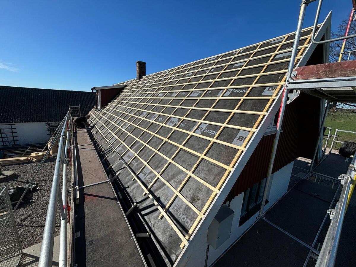 Underlagsduk och läkt färdigmonterad på tak med byggställning längs takfoten i soligt väder