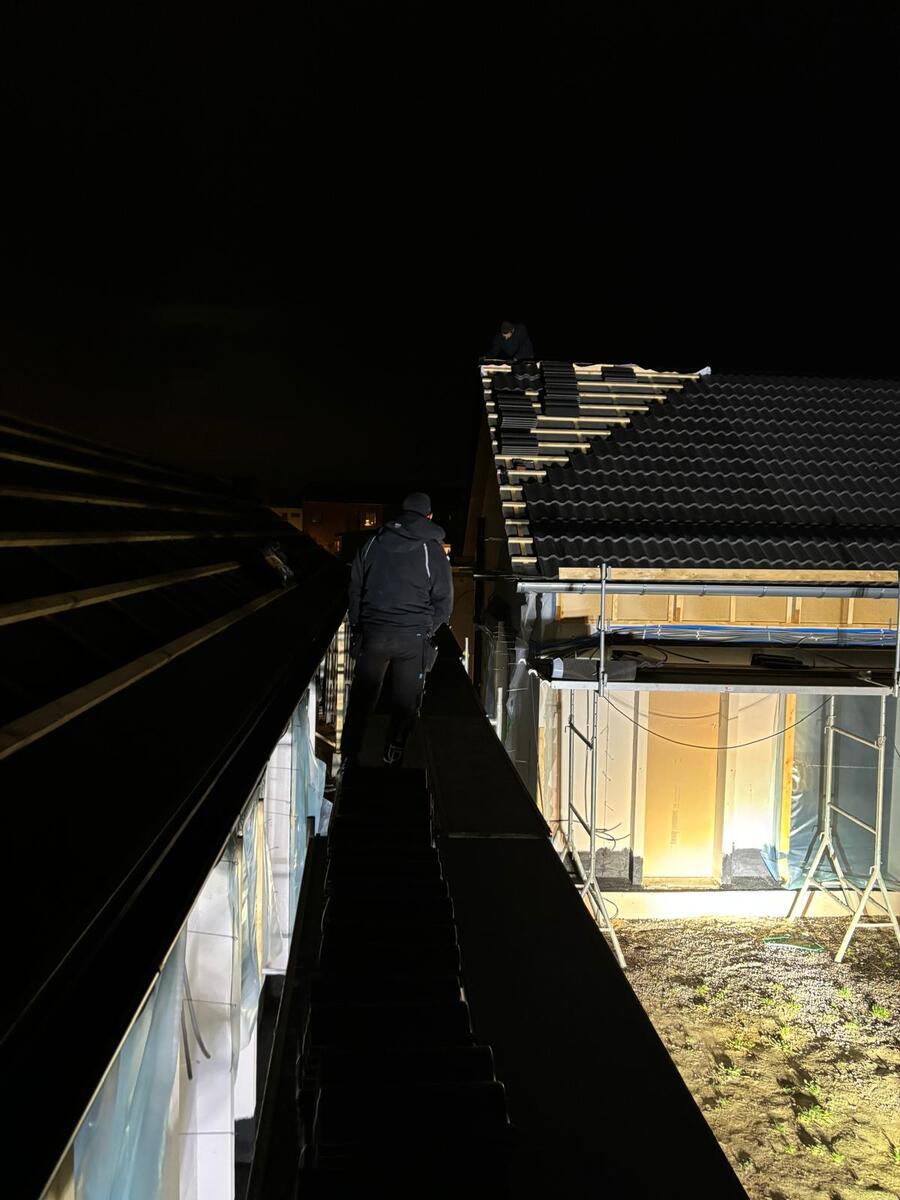 Takläggare inspekterar takstol och isolering sett underifrån i mörkt utrymme