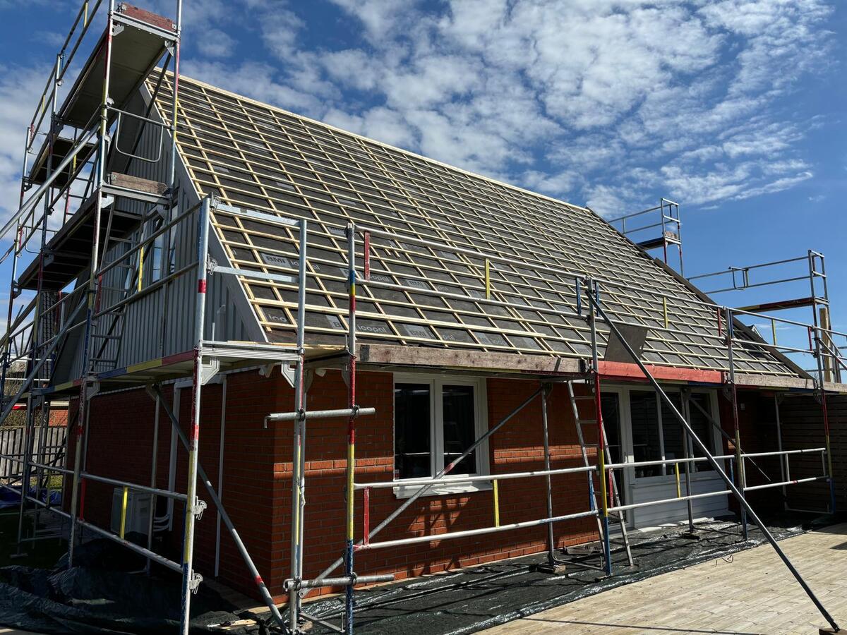 Villa under byggnation med grå takpannor och byggställning runt hela fastigheten