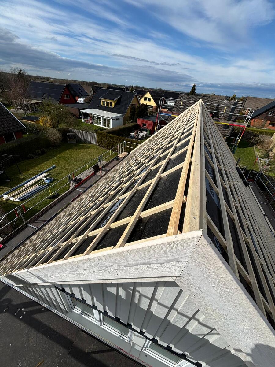 Ny träläkt monterad längs taknock på villa med byggställning och skånsk villabebyggelse i bakgrunden