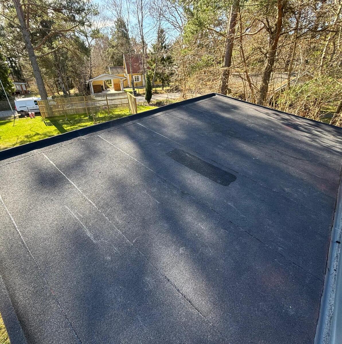 Färdiglagt platt tak med svart tätskiktsmatta på villa omgiven av träd