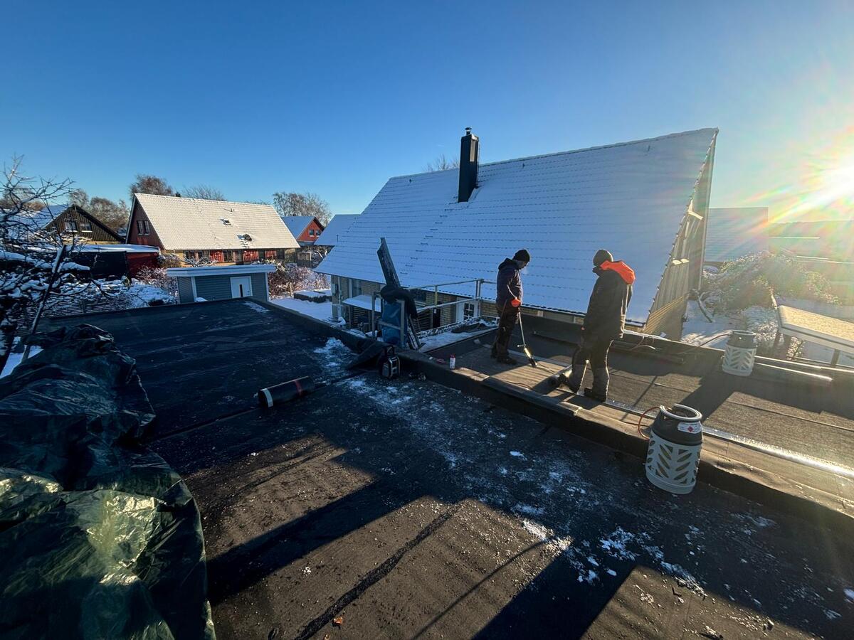 Två takläggare arbetar på platt tak med rivningsmaterial i vintermiljö och soligt väder