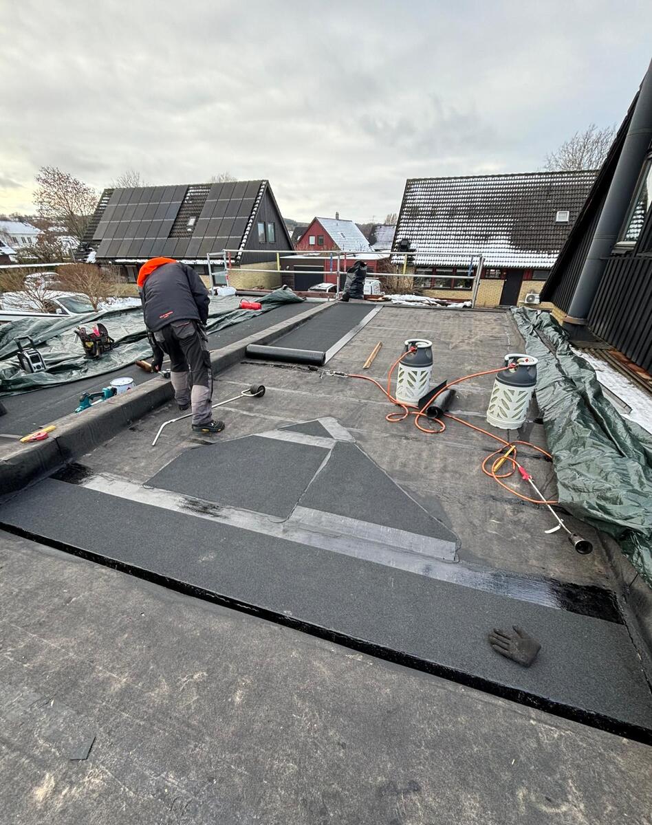 Takläggare svetsar tätskiktsmatta på platt tak med gasolverk i vintermiljö