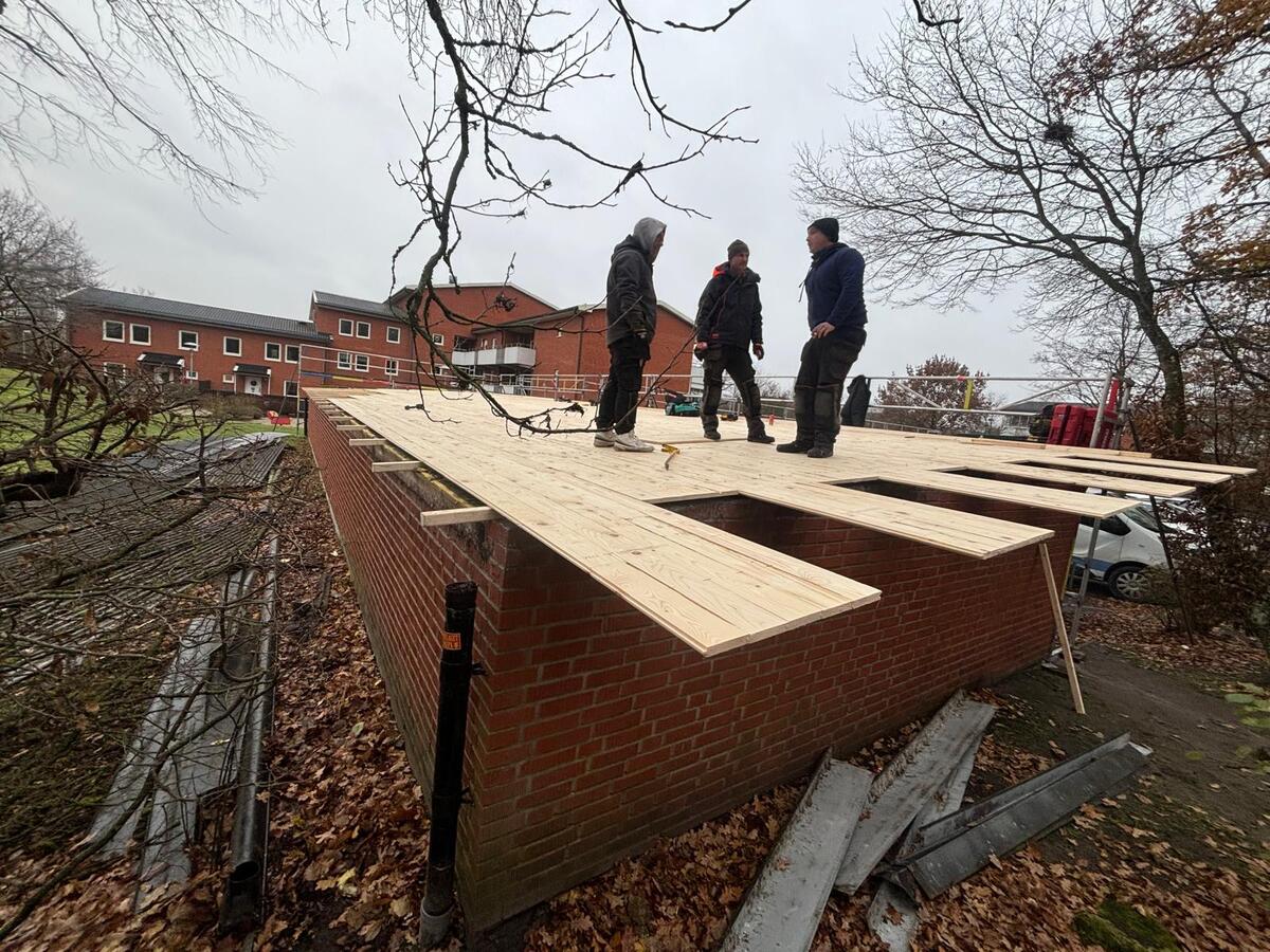 Tre takläggare inspekterar ny råspont på flackt tak på tegelbyggnad under höst