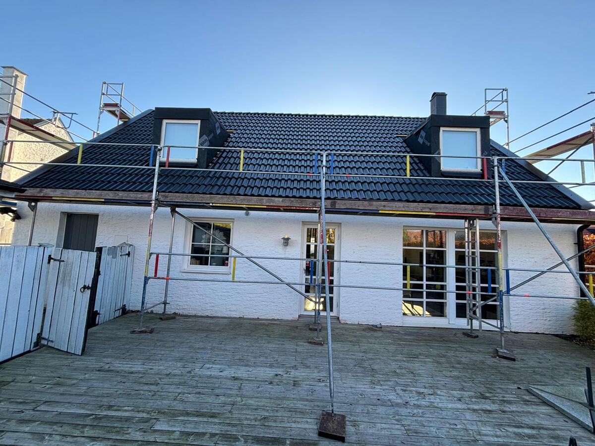 Färdiglagt tak med svarta betongtakpannor och takkupor på vit villa med byggställning