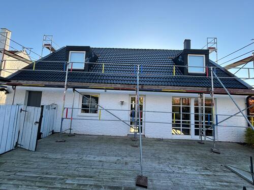 Färdiglagt tak med svarta betongtakpannor och takkupor på vit villa med byggställning
