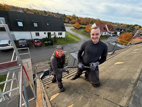 Två glada takläggare från TAK Skåne poserar på tak i villaområde under höst
