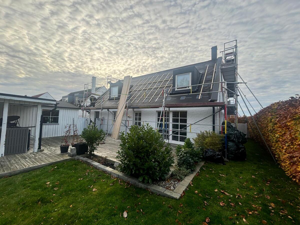 Vit villa med pågående takläggning och byggställning sett från trädgården i mulet väder