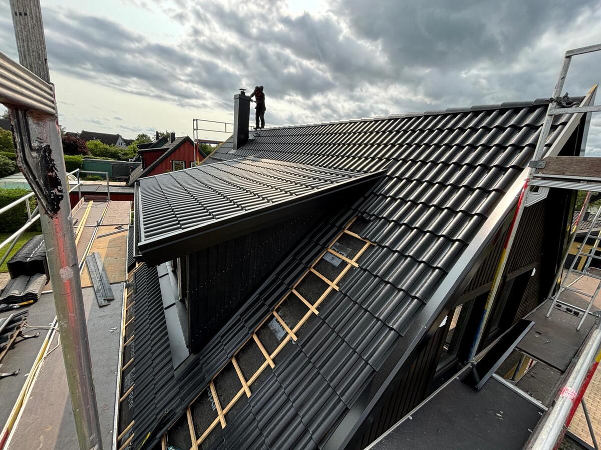 Pågående takbyte med svarta betongtakpannor och synlig läkt på angränsande takyta med byggställning