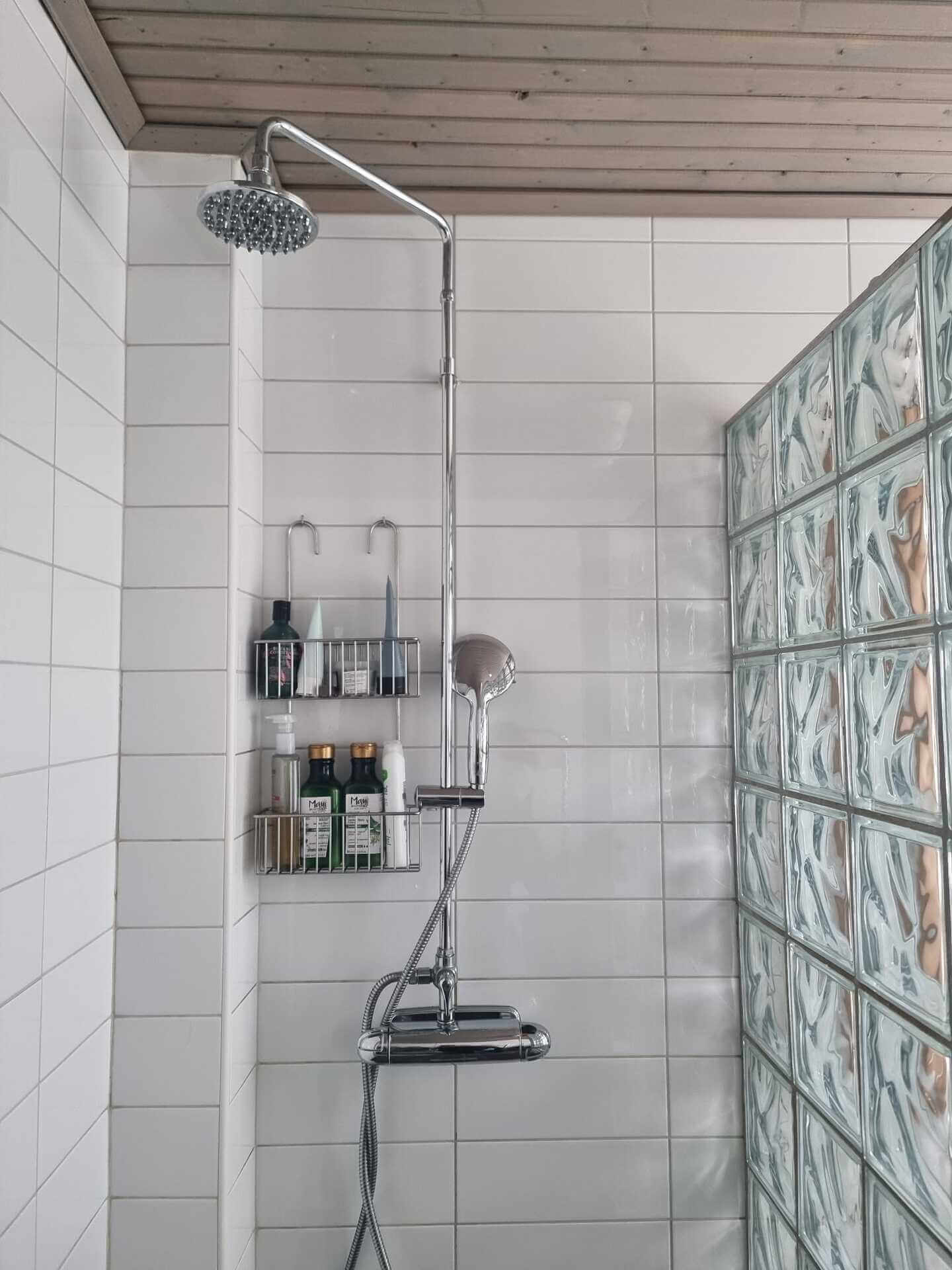 Rengjord duschkabin med vita kakelplattor och duschställning med hylla