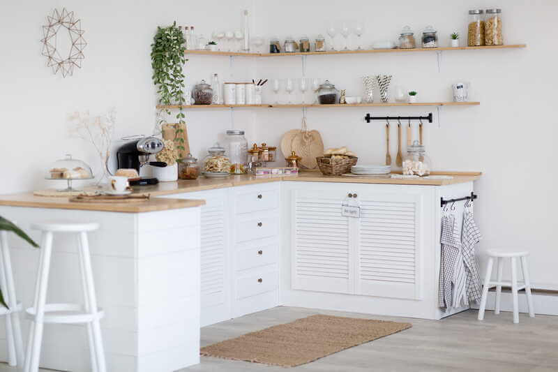 Vitt lantligt kök med träbänkskiva, öppna hyllor och kaffebryggare