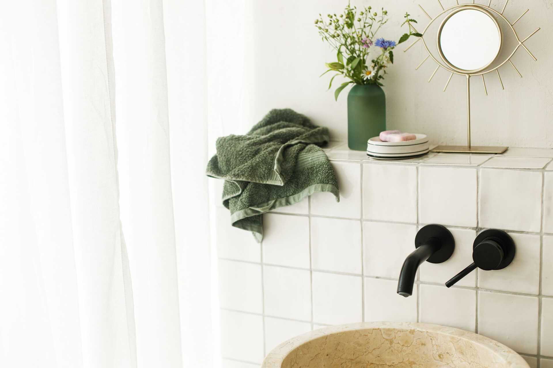 Minimalistiskt badrum med vita kakelplattor, svarta kranar och gröna växter