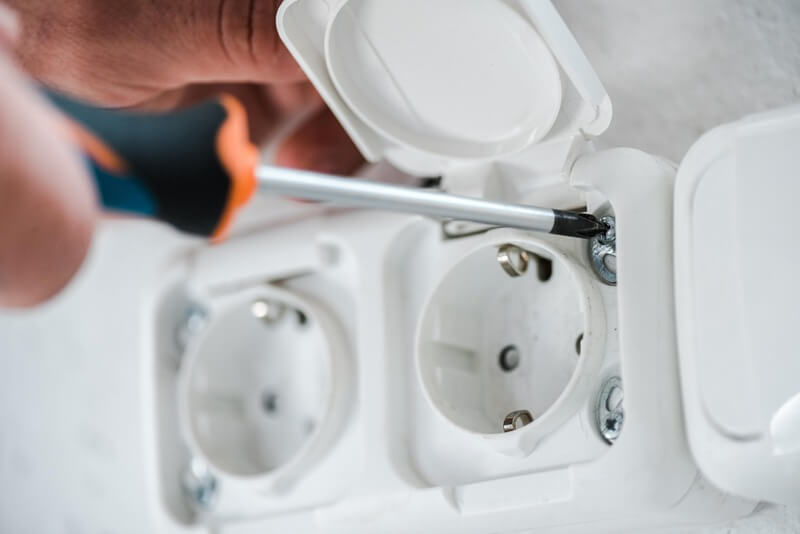 Elektriker installerar eluttag i vägg med skruvmejsel