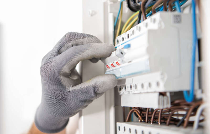 Elektriker med skyddshandskar justerar brytare i elcentral