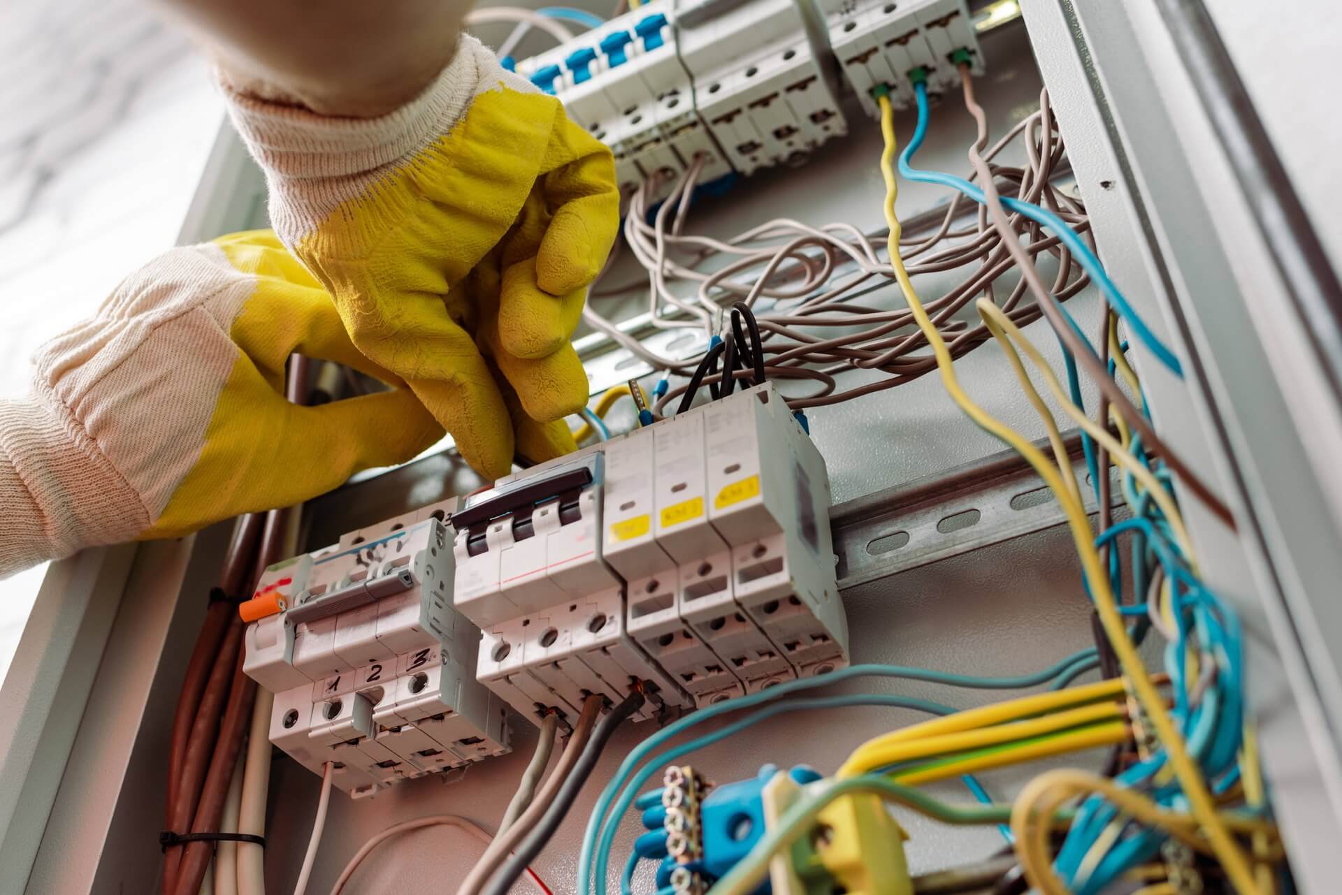 Elektriker med gula handskar arbetar i elcentral med kablar och säkringar