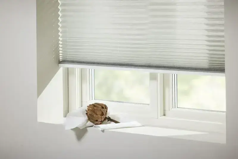 Beige plisségardin nedfälld över fönster med dagsljus