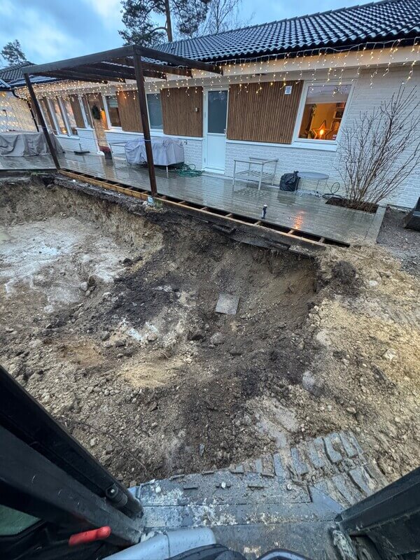 Djup schaktgrop inför poolbygge under trädäck