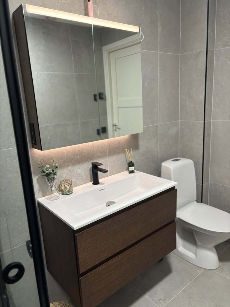 Renoverat badrum med tvättställ på mörk kommod, spegel och toalett